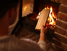A hand putting a piece of wood into a fire in a fireplace