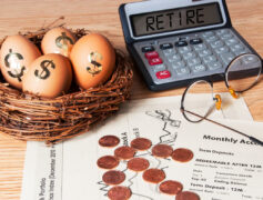 Retirement planning: a calculator that says "retire" where the numbers should be, a nest with eggs that have dollar signs on them and pennies in the shape up an up arrow on top of some retirement paperwork.