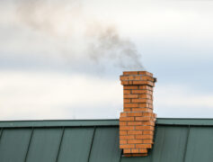 Roof and chimney with smoke coming out of the chimney. Common chimney problems can cause issues during a home sale.