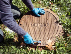 Septic maintenance, man reaching for a septic manhole cover.