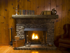 Beautiful fireplace burning logs in a room with wood paneling.